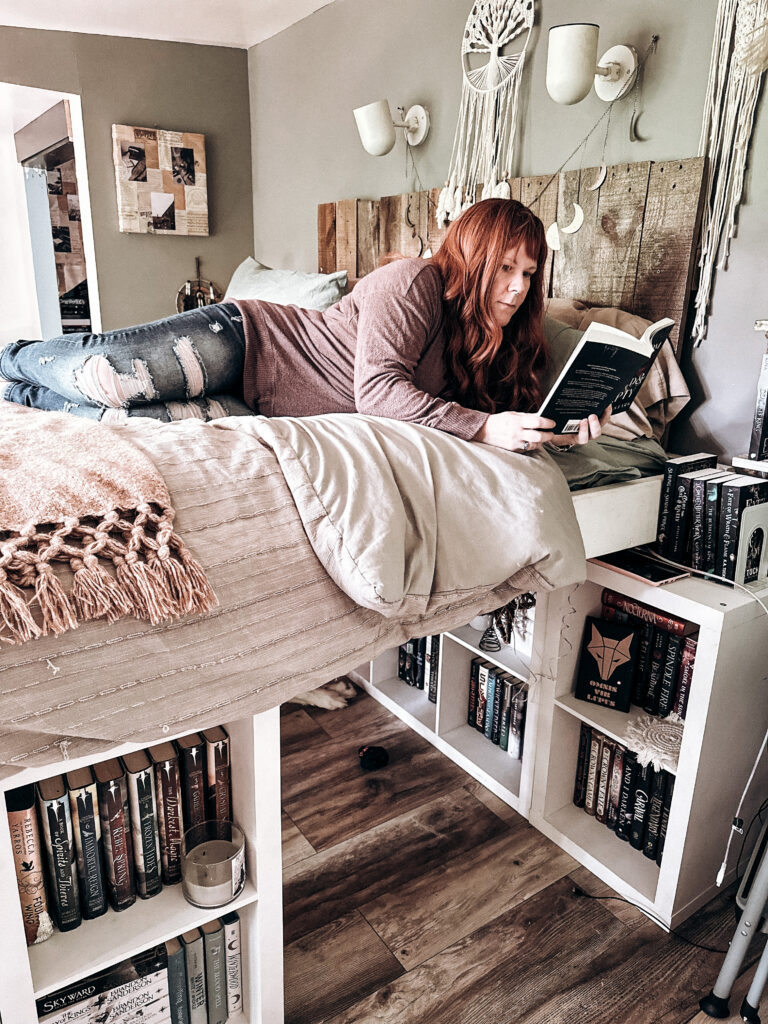 Woman reading a book on a custom bookshelf bed surrounded by books.